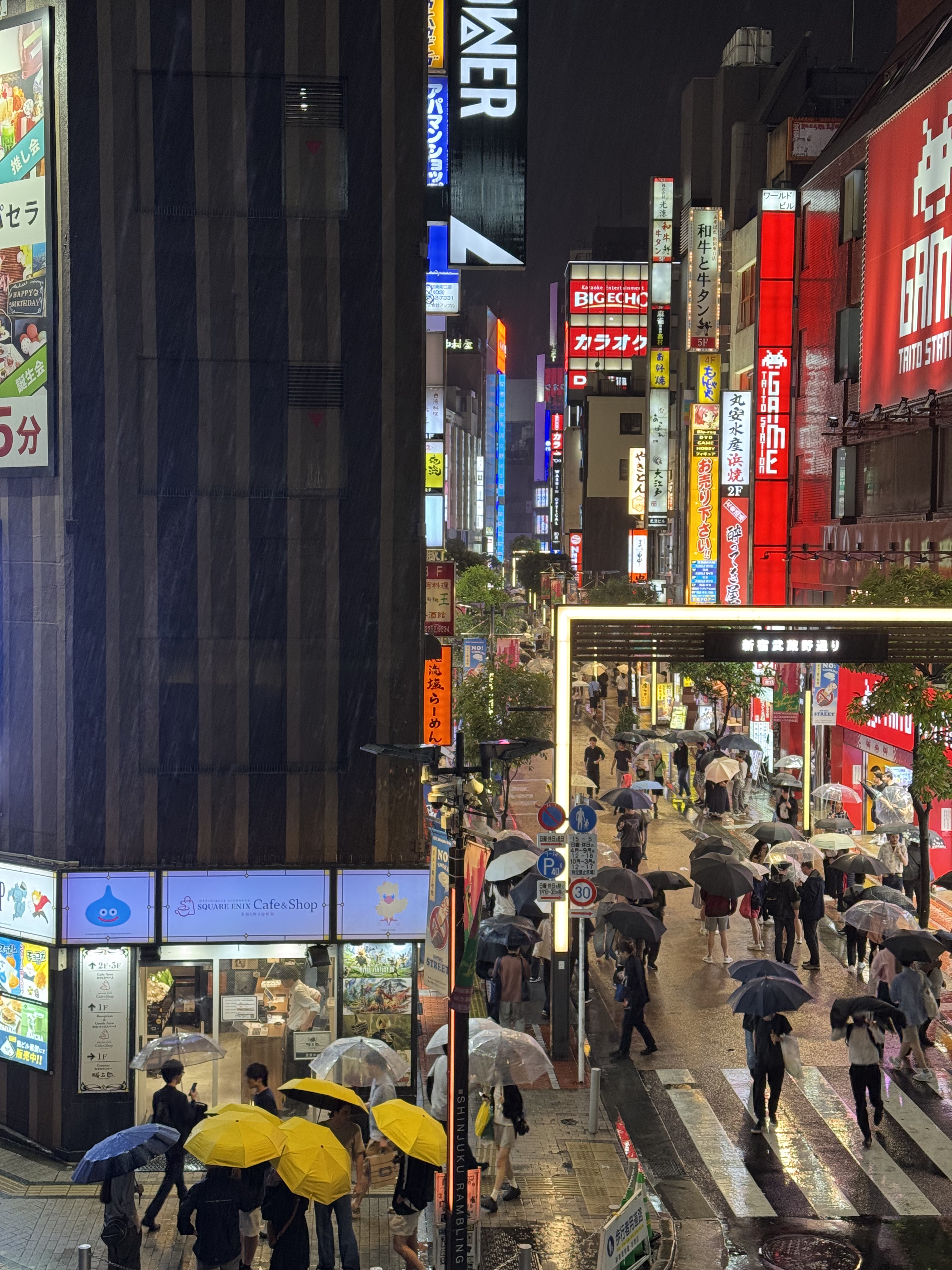 Einkaufsstraße in Shinjuku mit Leuchtreklamen und Menschen mit Regenschirm